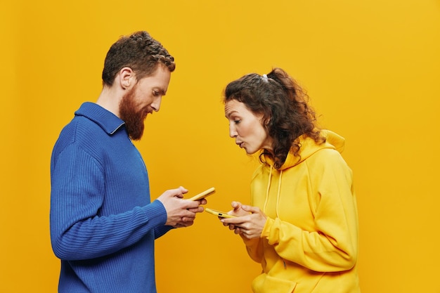 Woman man cheerful couple with phones in hand social networking and communication crooked smile fun and fight in yellow background The concept of real family relationships freelancers work online