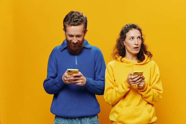 Woman man cheerful couple with phones in hand social networking and communication crooked smile fun and fight in yellow background The concept of real family relationships freelancers work online