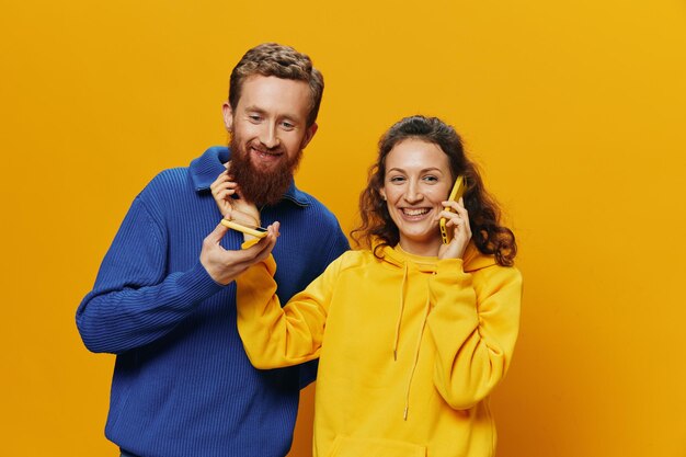 Woman and man cheerful couple with phones in hand talking on cell phone crooked smile cheerful on yellow background the concept of real family relationships talking on the phone work online