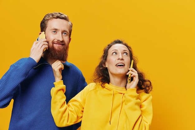 Woman and man cheerful couple with phones in hand talking on cell phone crooked smile cheerful on yellow background The concept of real family relationships talking on the phone work online