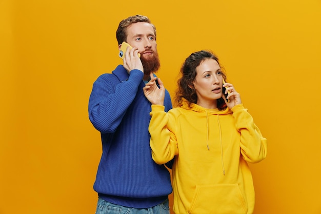 Woman and man cheerful couple with phones in hand talking on cell phone crooked smile cheerful on yellow background the concept of real family relationships talking on the phone work online