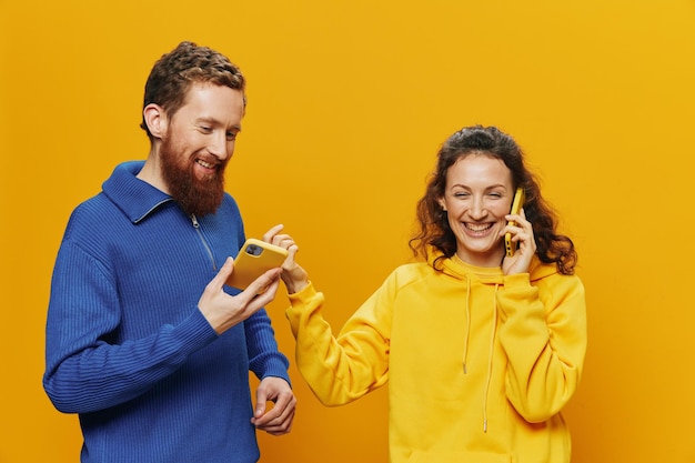 Woman and man cheerful couple with phones in hand talking on cell phone crooked smile cheerful on yellow background the concept of real family relationships talking on the phone work online