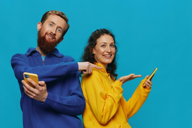 Woman and man cheerful couple with phones in their hands crooked smile cheerful on blue background the concept of real family relationships talking on the phone work online