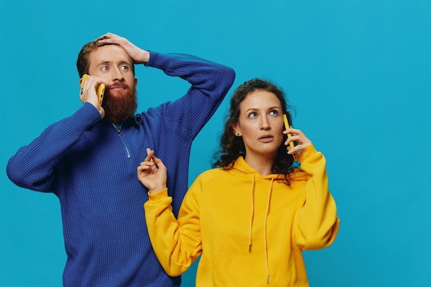 Foto coppia allegra donna e uomo con telefoni in mano sorriso storto allegro su sfondo blu il concetto di relazioni familiari reali che parlano al telefono funziona online