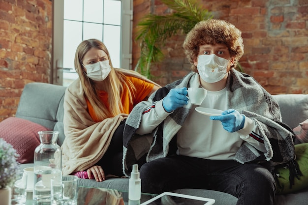 Photo woman and man, couple in protective masks and gloves isolated at home with coronavirus respiratory symptoms such as fever, headache, cough. healthcare, medicine, quarantine, treatment concept.