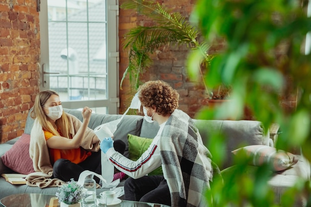 Woman and man couple in protective masks and gloves isolated at home with coronavirus