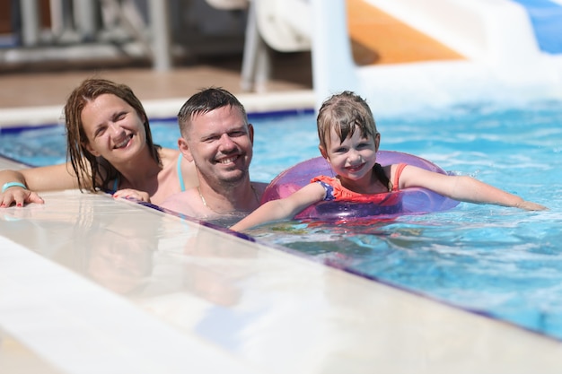 Foto donna, uomo e figlia sorridono insieme. famiglia nuotare in piscina al sole.