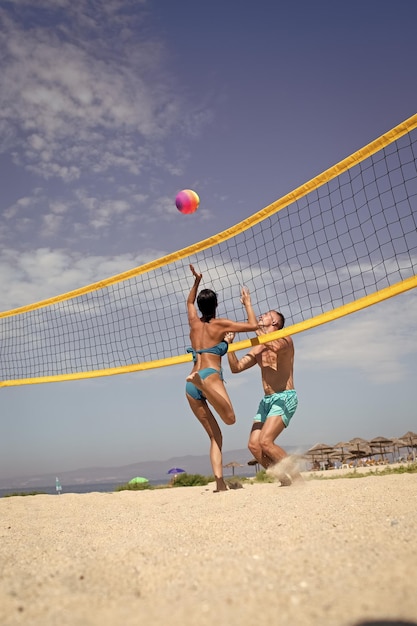 Donna e uomo in forma, forti, sani, che fanno sport sulla spiaggia. concetto di beach volley. le coppie si divertono giocando a pallavolo. la giovane coppia sportiva e attiva ha battuto la pallavolo, gioca.