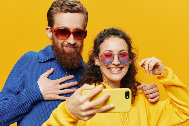 Woman and man funny couple with phones hand social networking and communication crooked do selfies smile fun on yellow background the concept of real family relationships freelancers work online