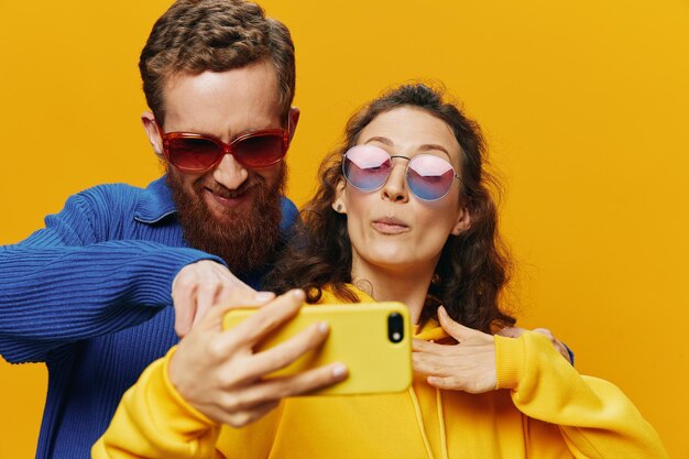 Woman and man funny couple with phones hand social networking and communication crooked do selfies smile fun on yellow background the concept of real family relationships freelancers work online