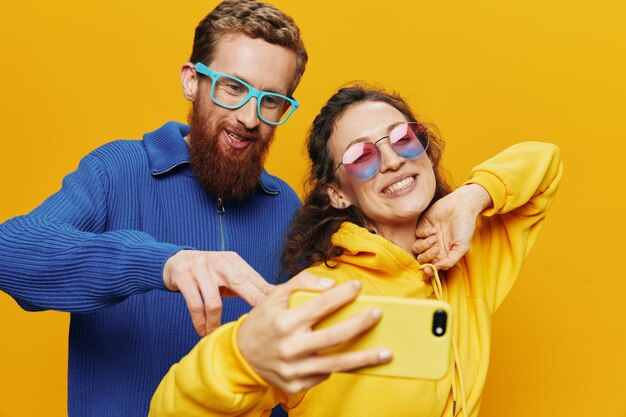 Woman and man funny couple with phones hand social networking and communication crooked do selfies smile fun on yellow background the concept of real family relationships freelancers work online