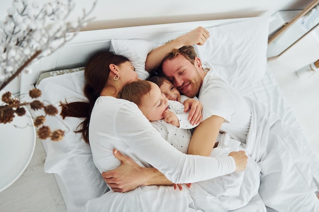 Woman and man lying down on bed with their children Interior and design of beautiful modern bedroom at daytime