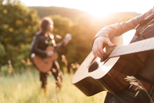 Woman and man playing acoustic guitar in nature at sunset