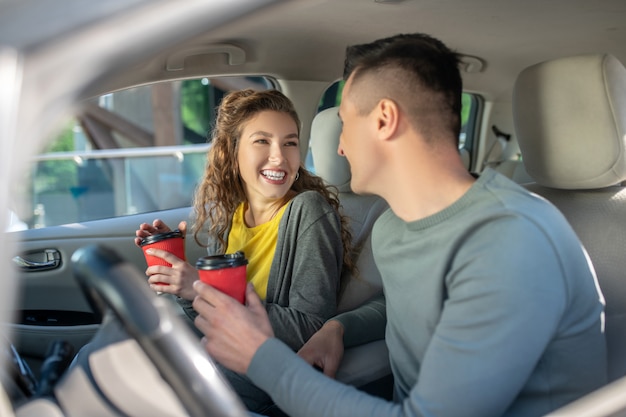 Woman and man sitting in car with glasses of coffee