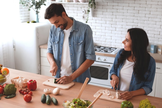 Woman and man slicing vegetables for salad on the kitchen