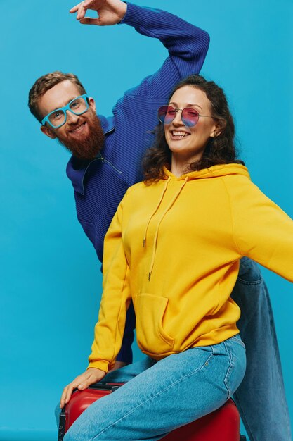 Woman and man smile sitting on suitcase with red suitcase smile on blue background packing for trip family vacation trip