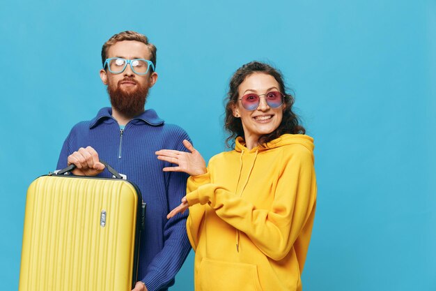 Photo woman and man smile sitting on suitcase with yellow suitcase smile on blue background packing for trip family vacation trip