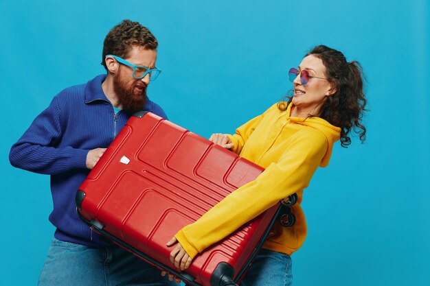 Photo woman and man smile suitcases in hand with yellow and red suitcase smile fun on blue background packing for a trip family vacation trip