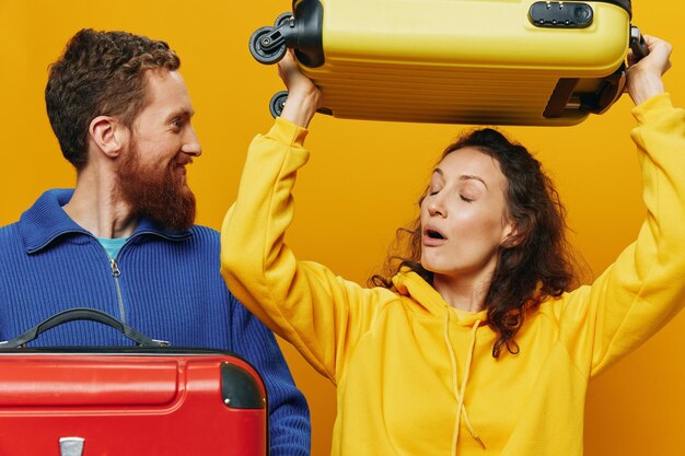 Photo woman and man smiling suitcases in hand with yellow and red suitcase smiling merrily and crooked yellow background going on a trip family vacation trip newlyweds