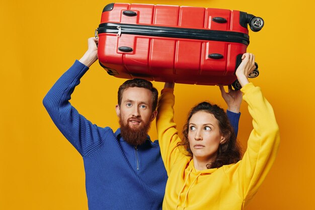 Woman and man smiling suitcases in hand with yellow and red suitcase smiling merrily and crooked yellow background going on a trip family vacation trip newlyweds