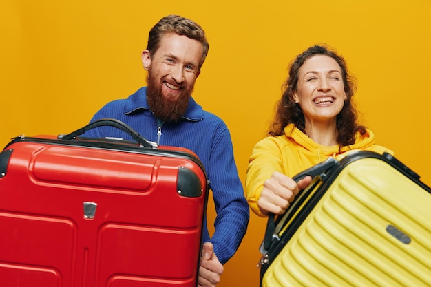 Woman and man smiling suitcases in hand with yellow and red suitcase smiling merrily and crooked yellow background going on a trip family vacation trip newlyweds