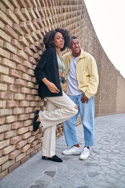 Woman and man standing leaning against brick wall