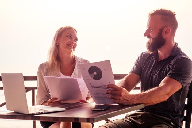 Woman and man in summer cafe by the sea working with laptop and charts schedule business partners abroad