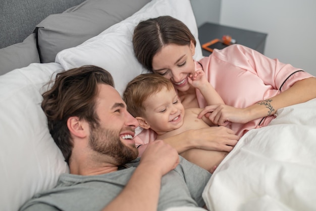 Woman and man touching baby lying on bed