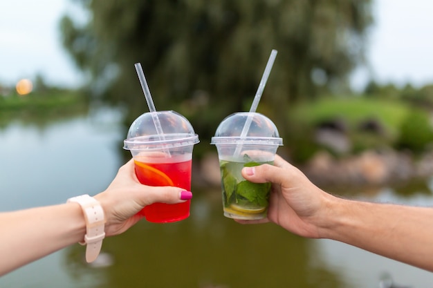 Woman and man during the walk holds in hands a fresh drink 