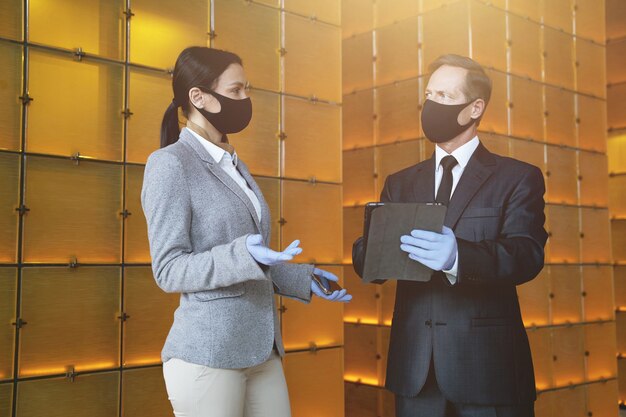 Woman and man wearing fabric masks and rubber gloves standing with modern devices and talking