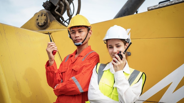 Woman manager and foreman using walkie talkie at side of cargo\
forklift in warehouse manager use tablet in white helmet safety\
supervisor in container custom terminal port concept import\
export