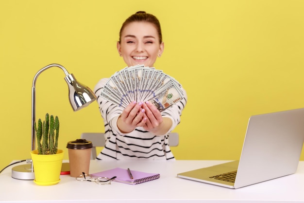 직장에 앉아 100달러 지폐를 손에 들고 있는 여성 매니저는 큰 이익에 만족한다