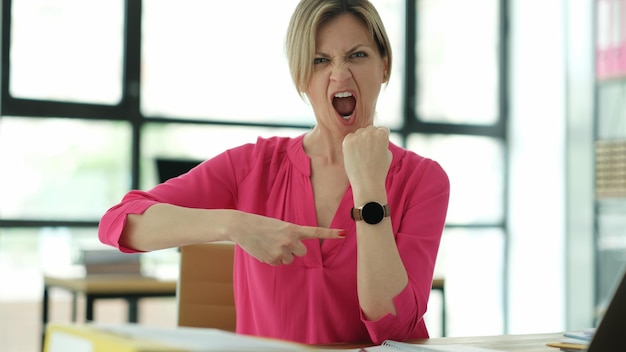 Woman manager screaming and pointing finger at wrist watch in office