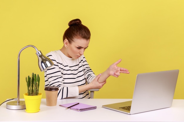 Woman manager sitting at workplace with laptop threatening and pointing finger gun to laptop screen