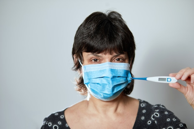 Woman in a mask reads temperature on a thermometer