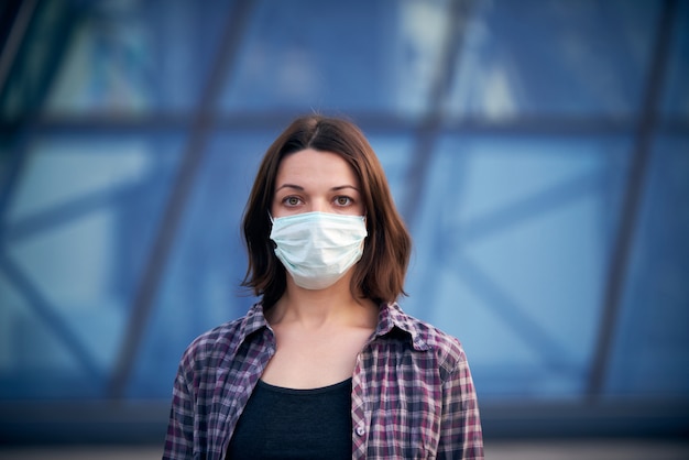 市でのコロナウイルスの流行のため、路上で仮面の女性。背景にモダンな建物。