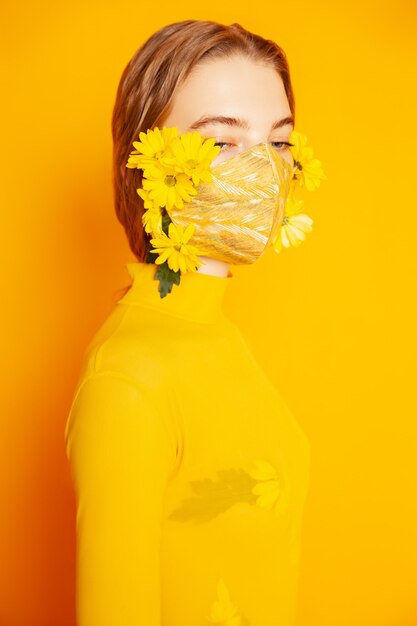 Woman in mask with yellow flowers in studio