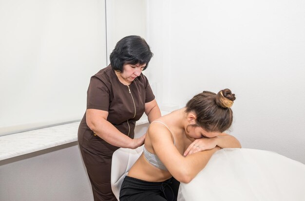 A woman massage therapist gives a back massage to a young girl in a massage parlor.