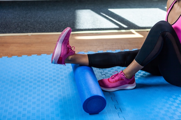 Woman massaging legs with massage roller after hard workout in fitness class