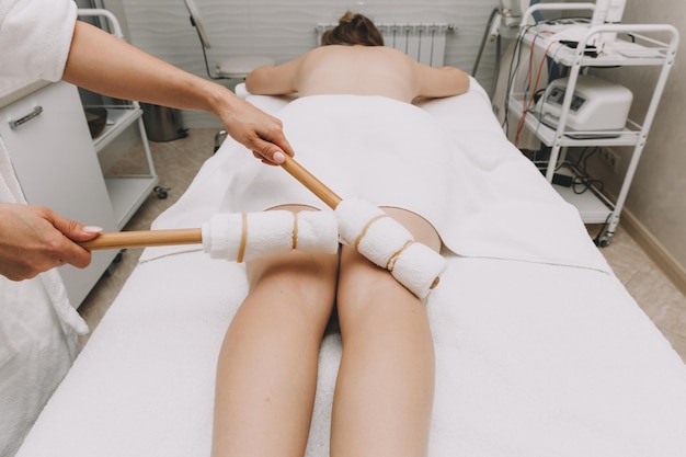 A woman masseur makes a massage of the legs and thighs with bamboo sticks