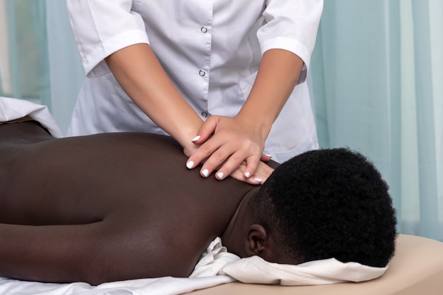 Woman masseuse doing massage of shoulder area to black man