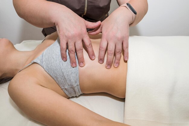 Woman masseuse massages belly of young girl client in massage parlor.