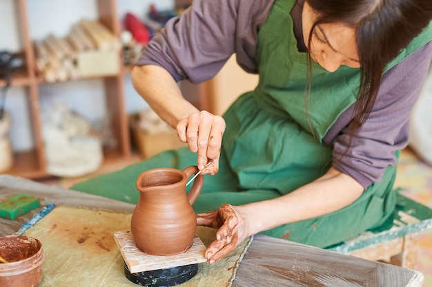 Woman master potter sculpts a jug of red clay in the workshop.