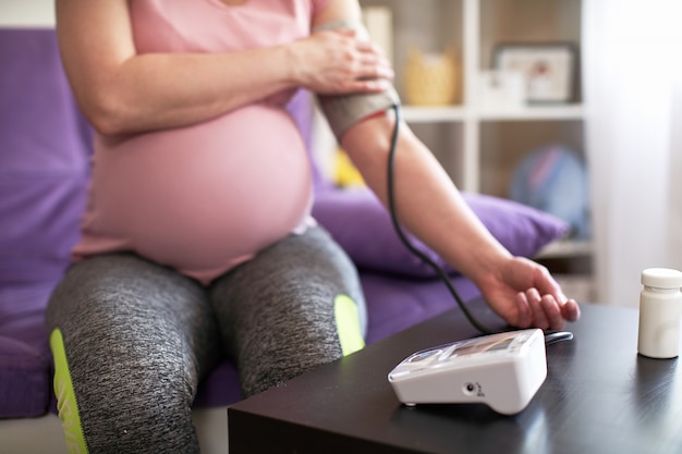 Una donna misura la pressione sanguigna con un manometro elettronico, mal di testa durante la gravidanza, cattiva salute. messa a fuoco selettiva su attrezzature mediche