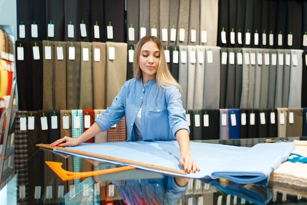 Woman measures the fabric in textile store. Shelf with cloth for sewing