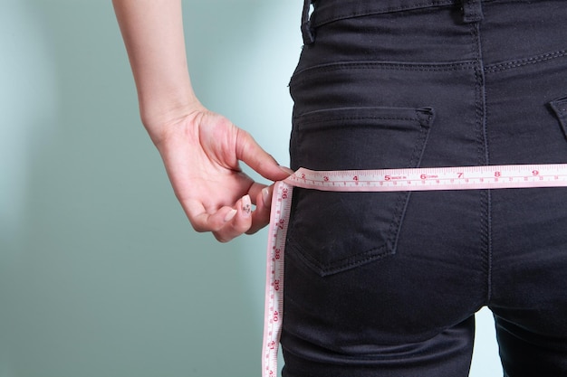 A woman measures her butt with a measuring tape