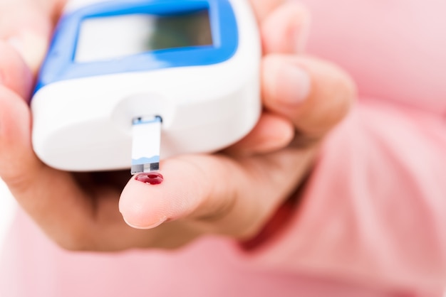 Woman measuring glucose level with glucometer