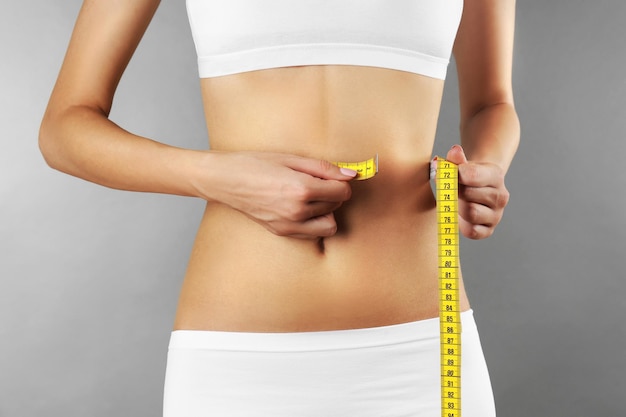 Woman measuring her waist on color background