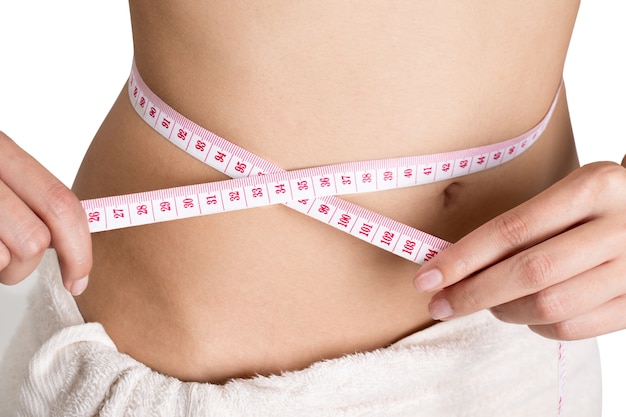 彼女のウエストを測定する女性は、体重を減らし、健康的な体のコンセプトを白い背景にします。