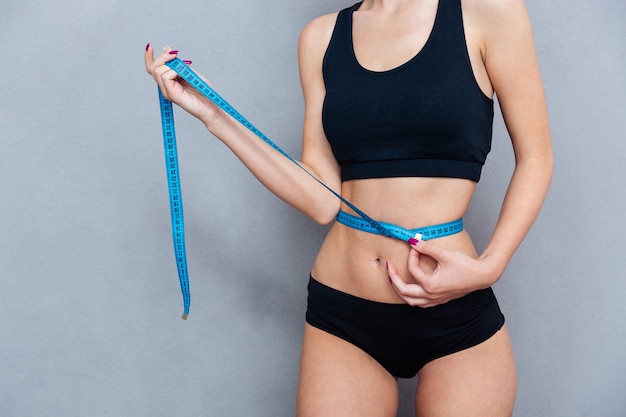 Woman measuring her waist with centimeter tape isolated on grey background